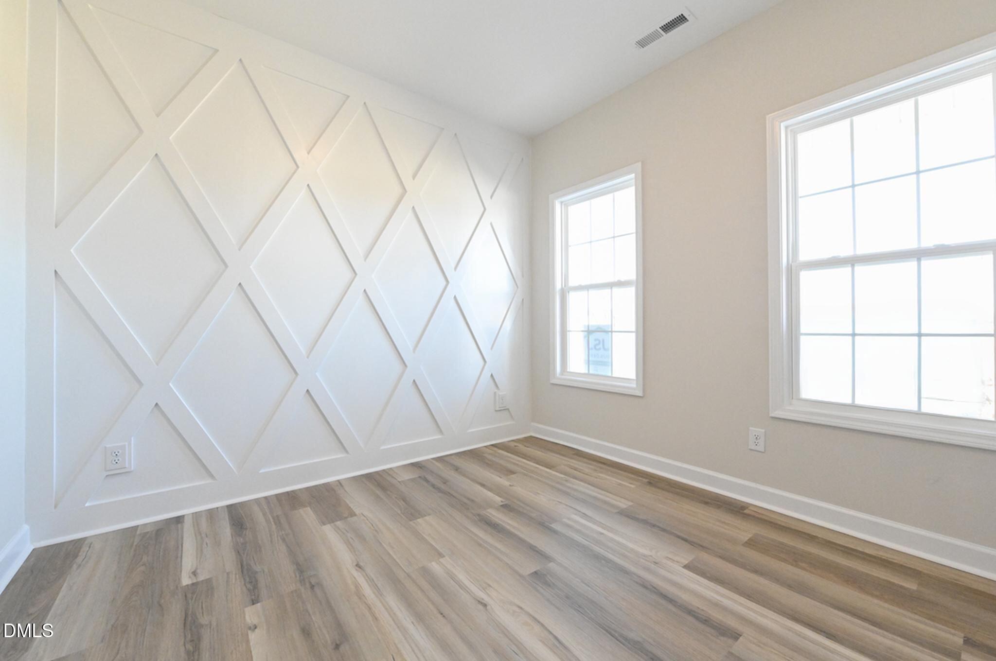 Vacant room with a geometric white feature wall, two windows, and gray plank flooring.