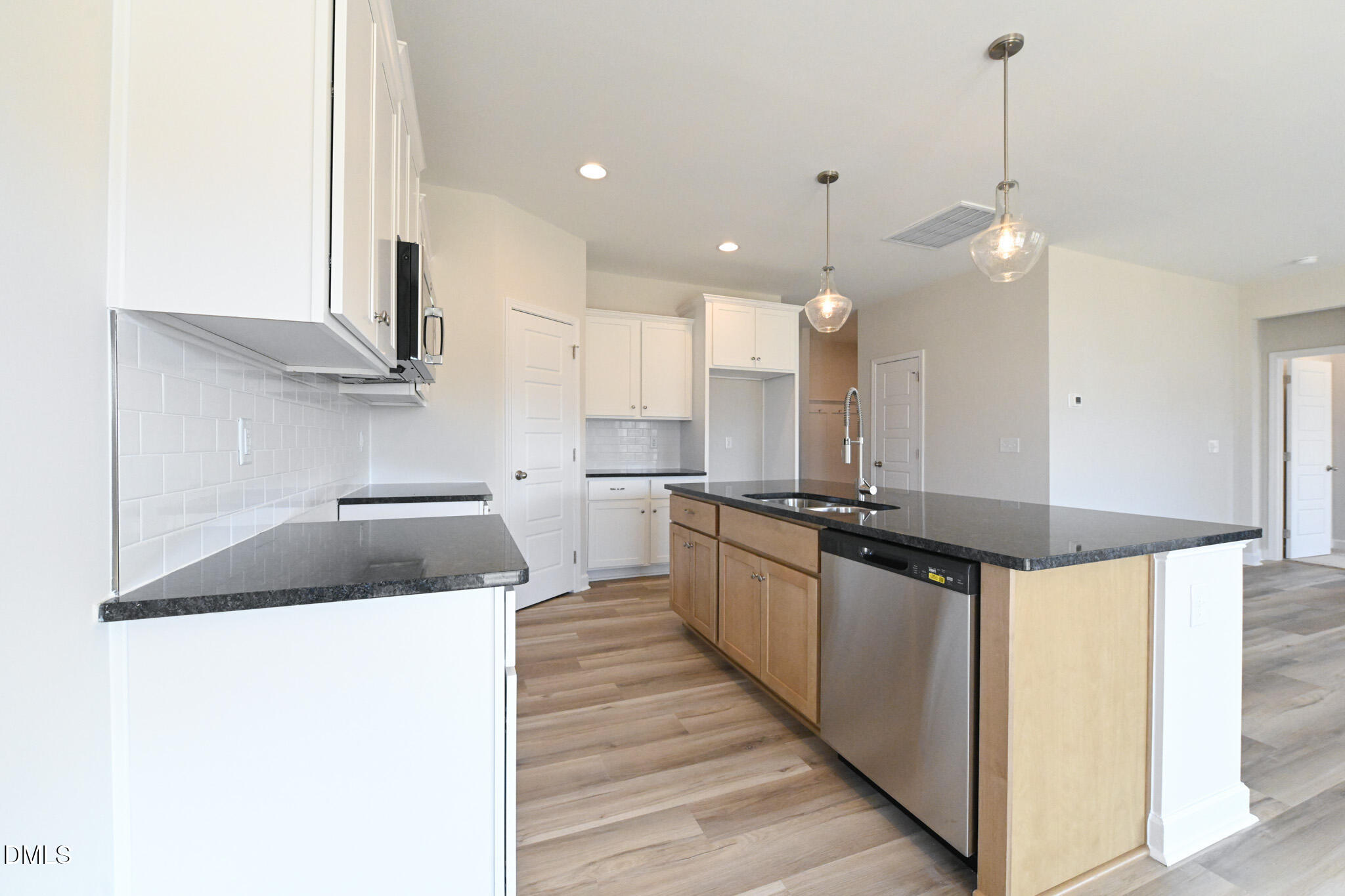 Vacant kitchen with a large wood-paneled island, dark countertops, and glass pendant lights.