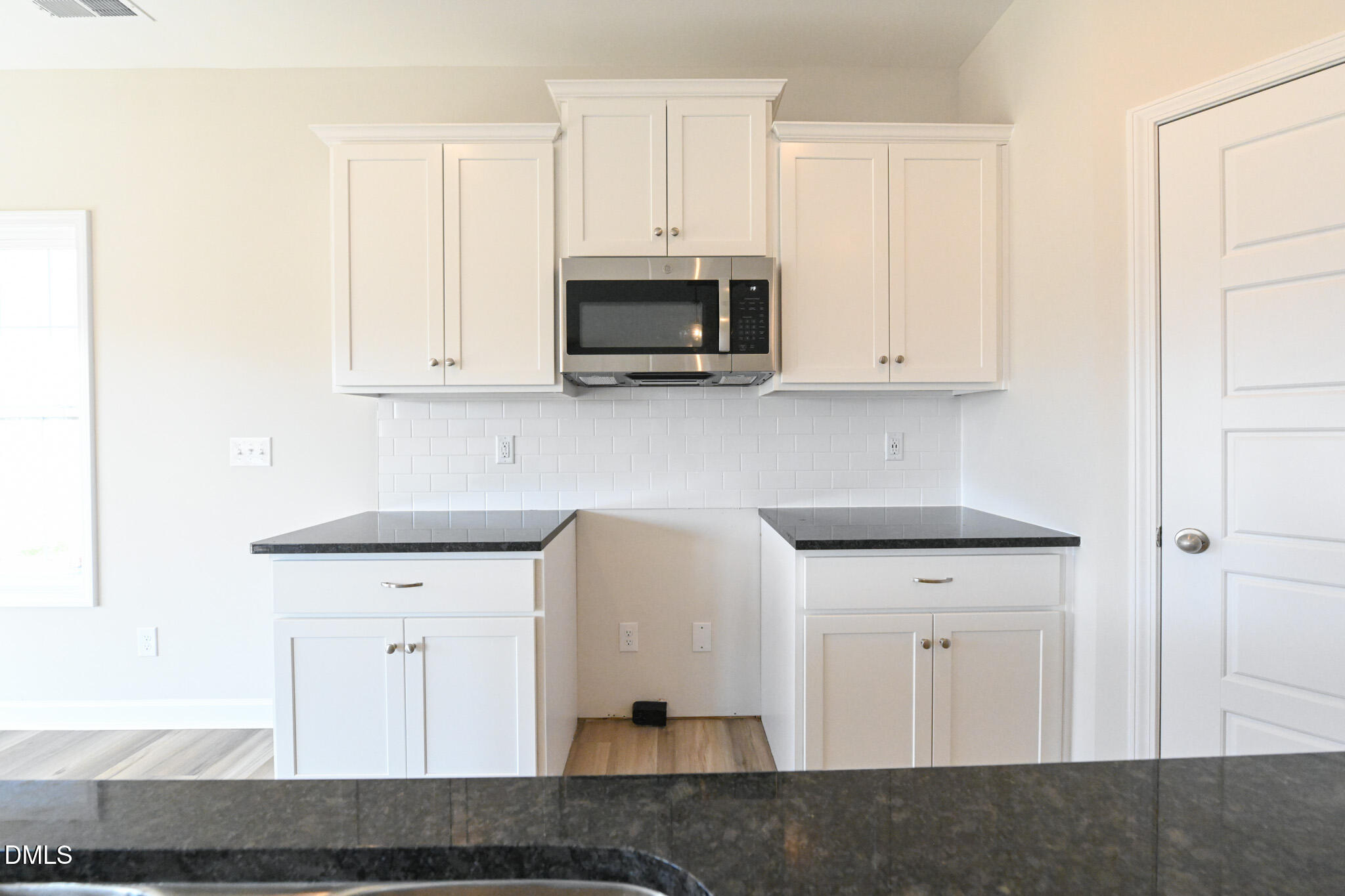 Vacant kitchen with white shaker cabinets, subway tile backsplash, and dark countertops.