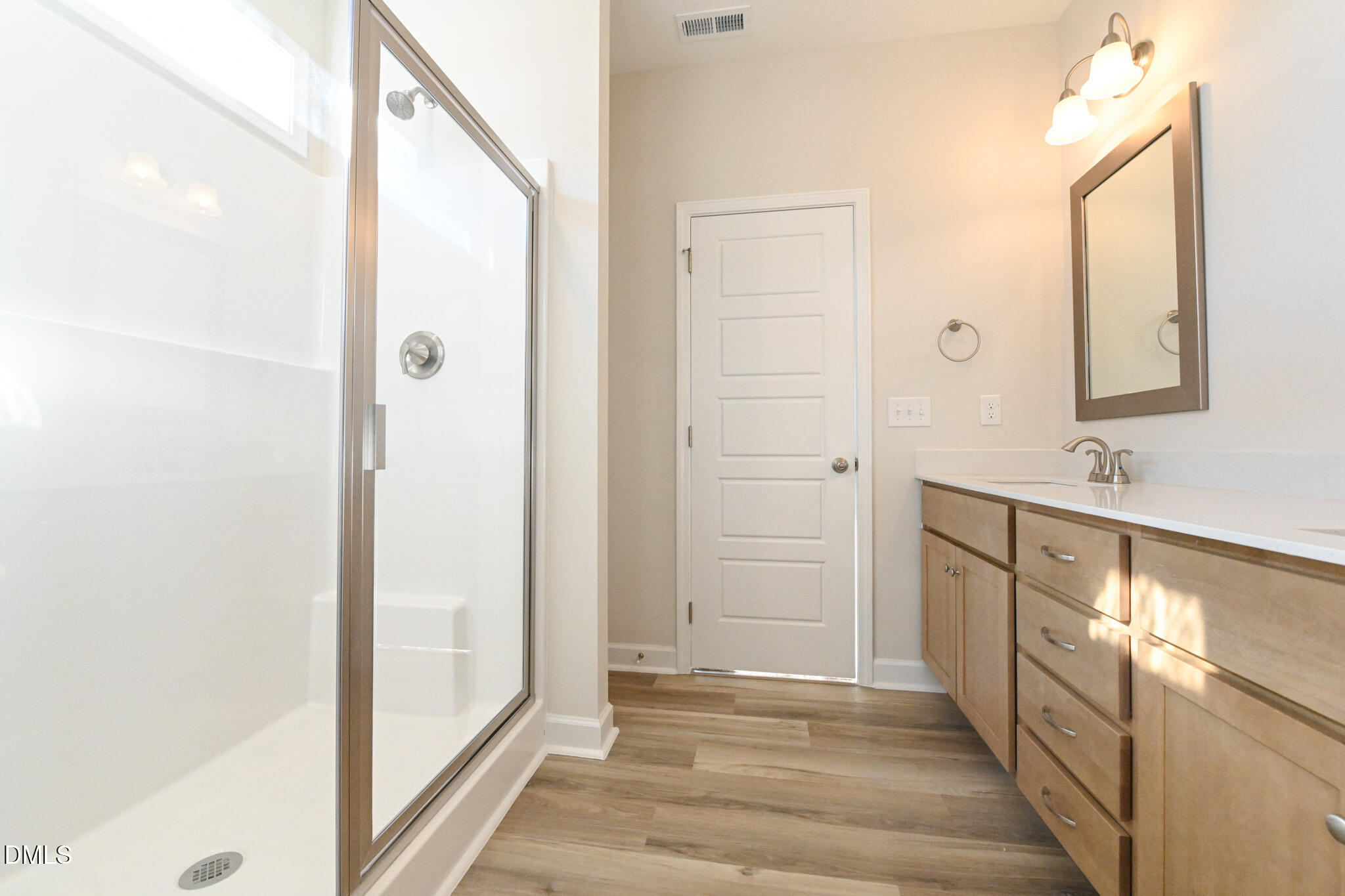 Bathroom with a glass shower and long wood-tone vanity with white countertop.