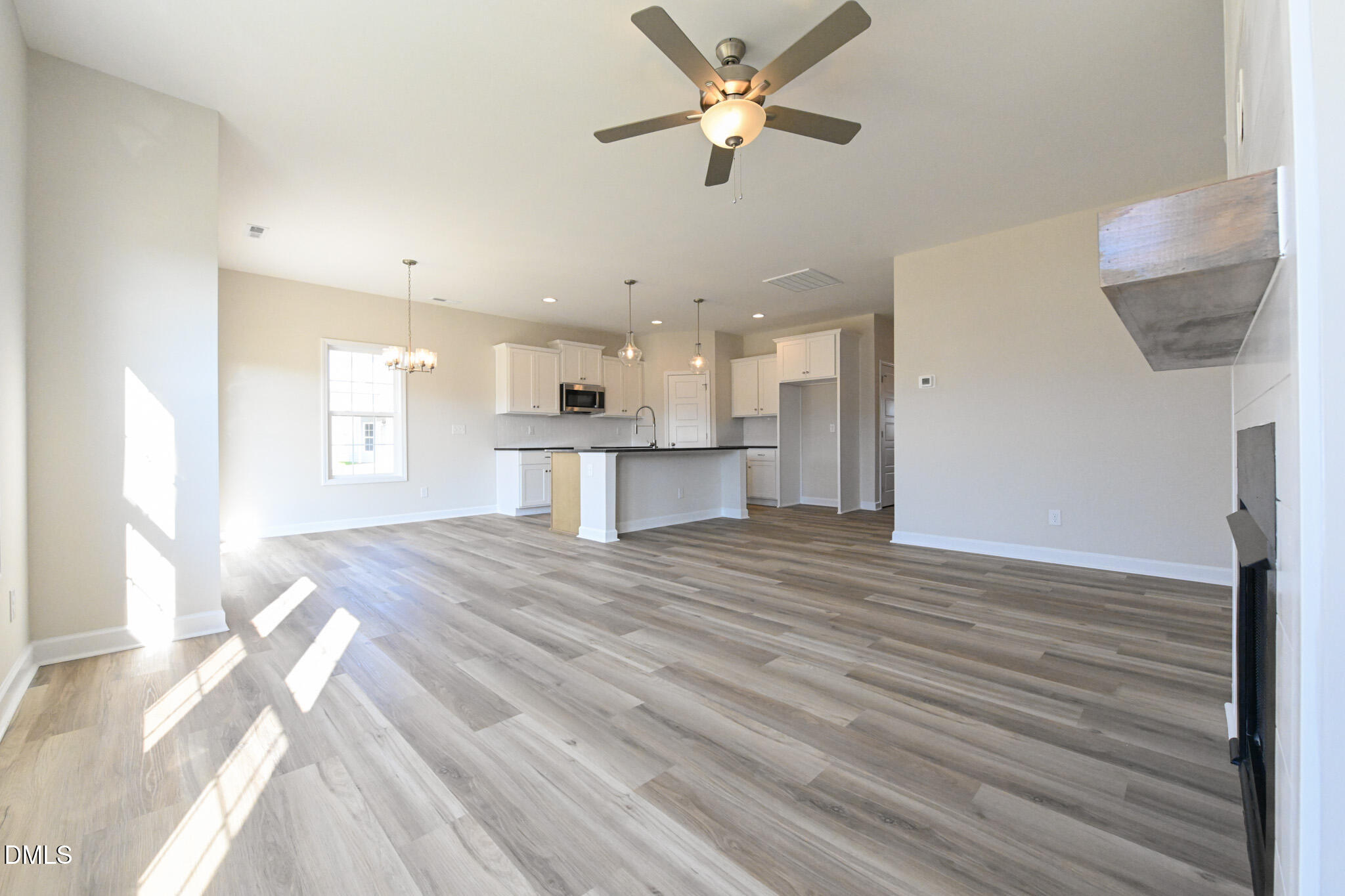 Vacant open-plan living room and kitchen with an island and sunlight across gray wood-look floors.