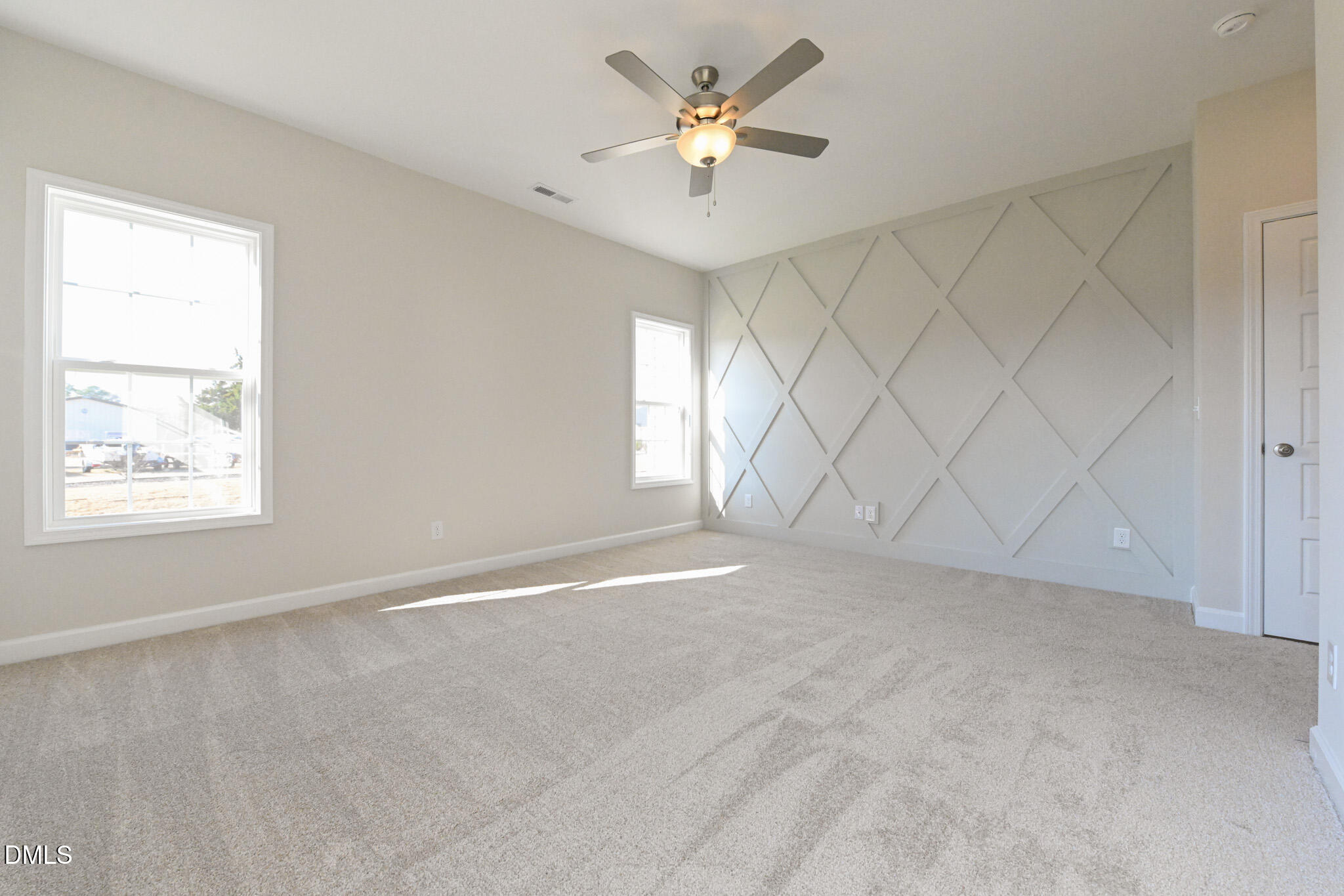 Empty bedroom with carpet, a ceiling fan, and a geometric accent wall.