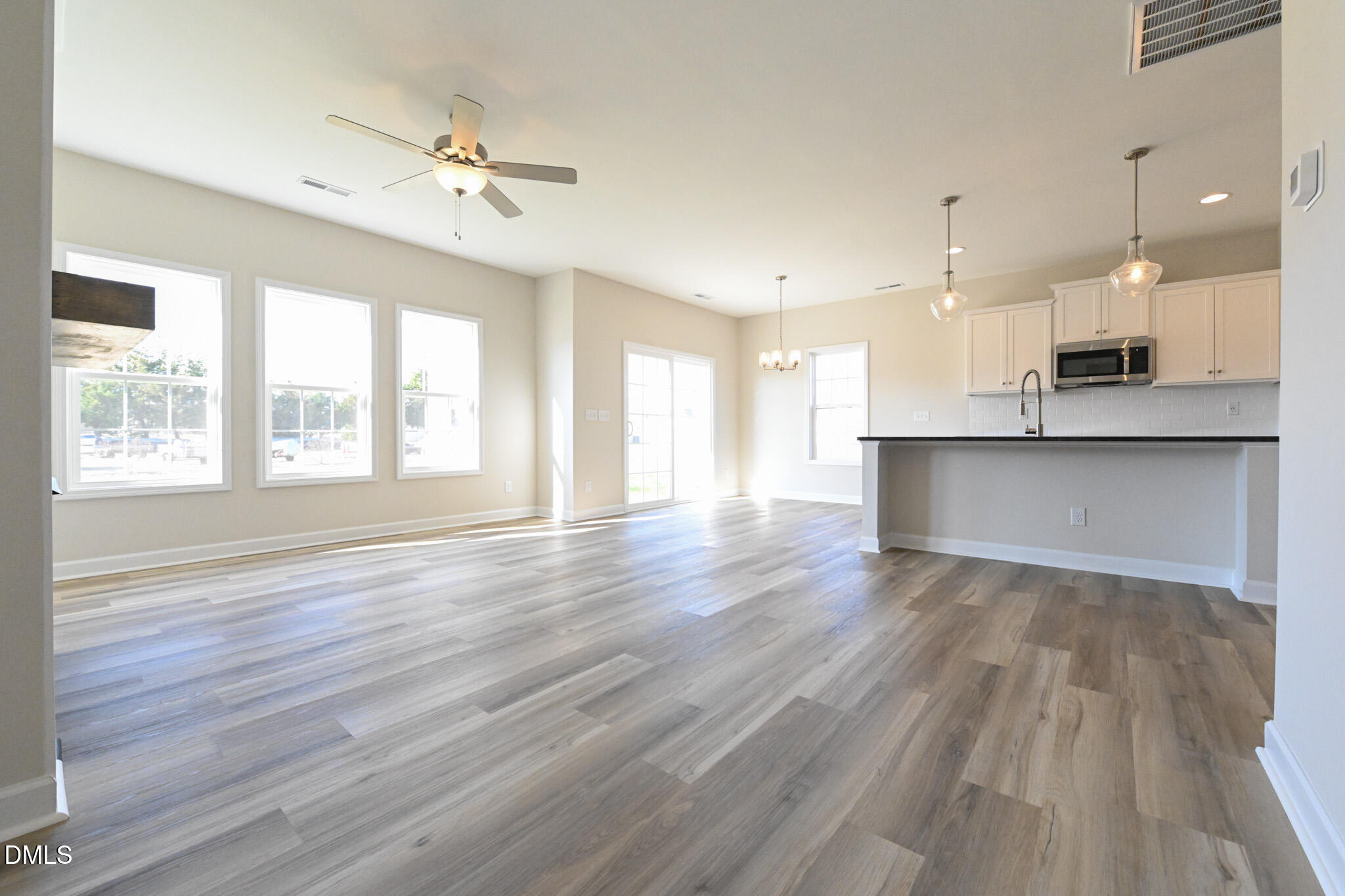 Vacant open-plan living area and kitchen with gray wood-look floors, large windows, and a breakfast bar.