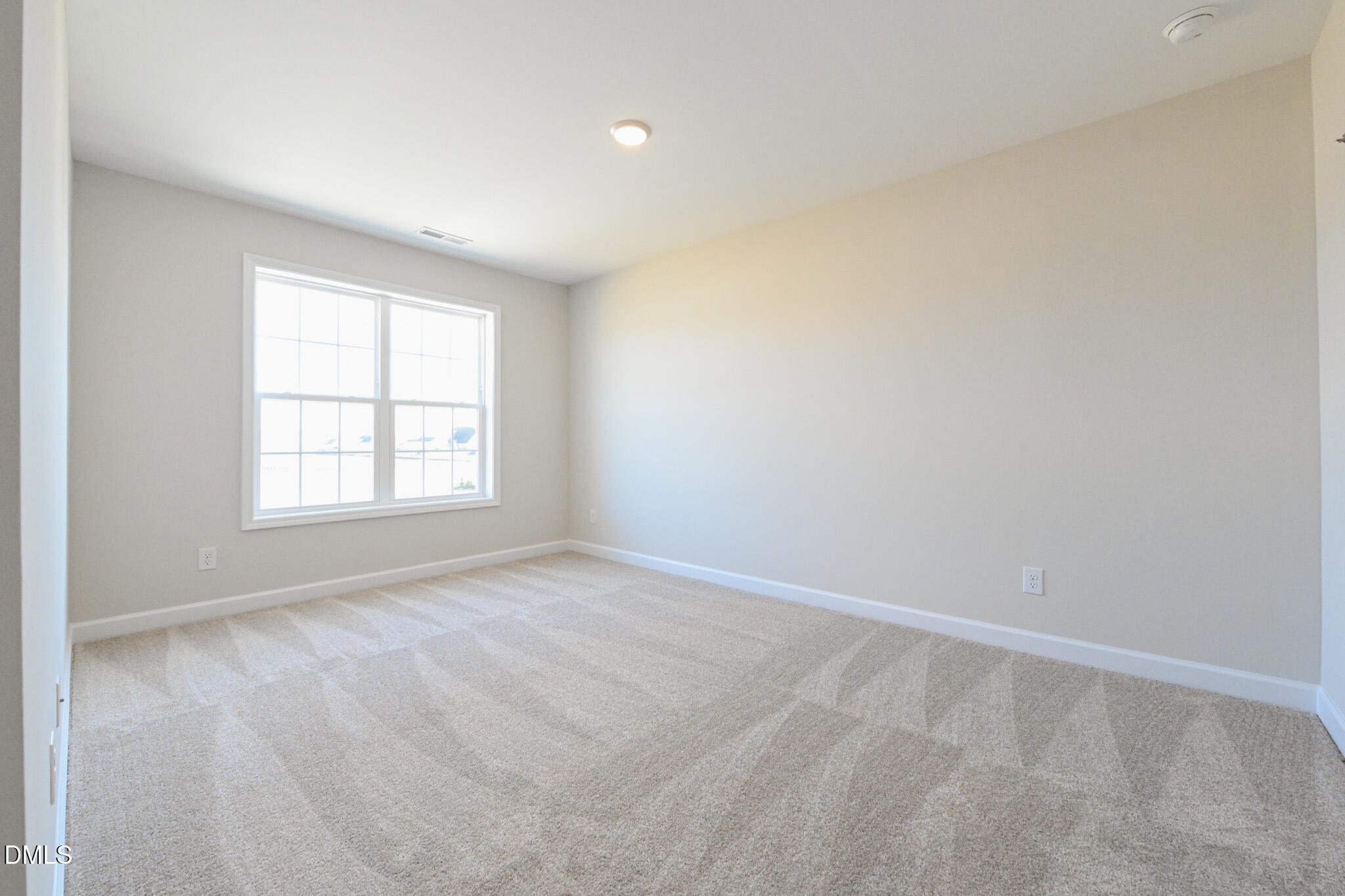Empty bedroom with beige carpet and a large double window.