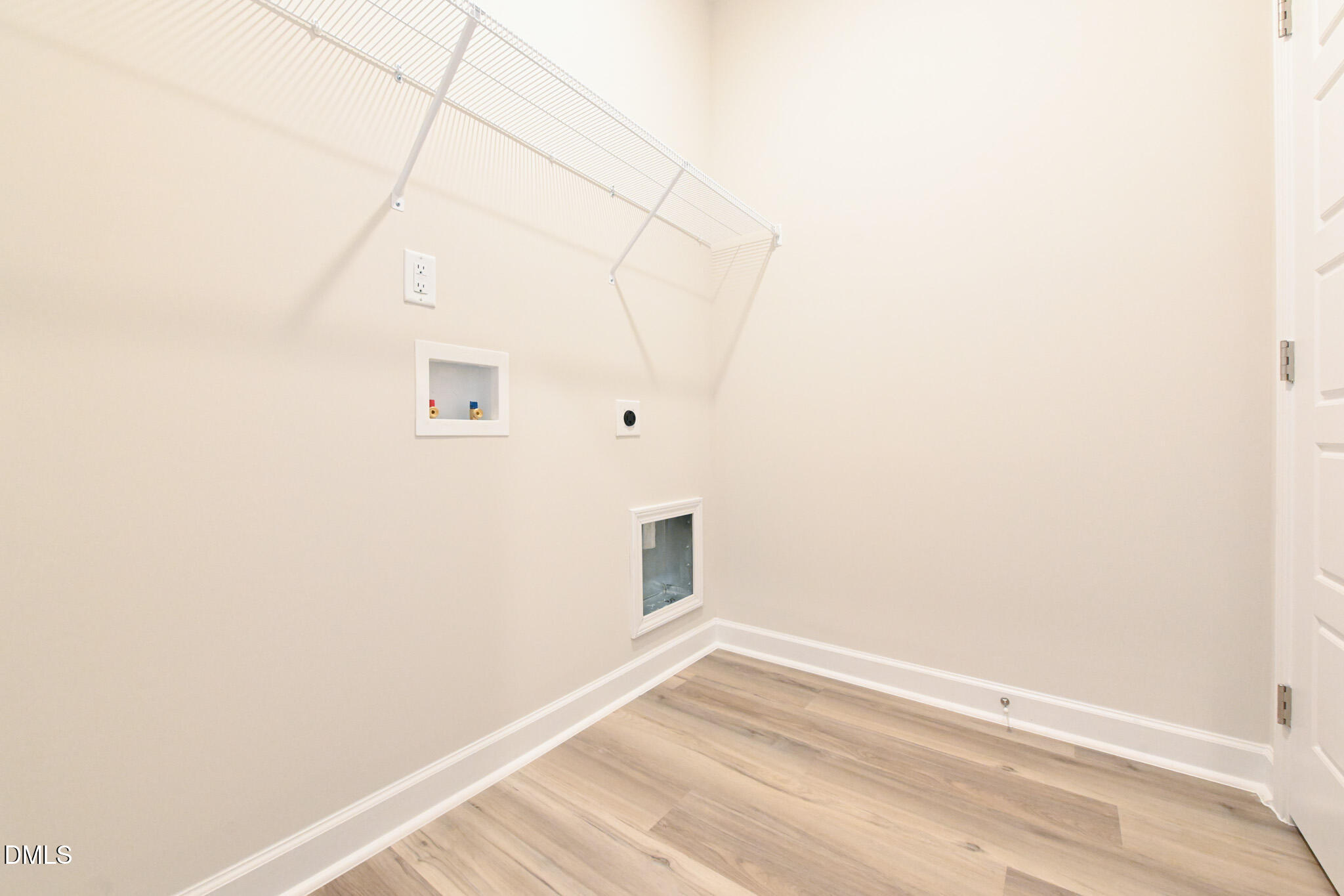 Empty laundry room with washer and dryer hookups, a wire shelf, and light wood-look flooring.