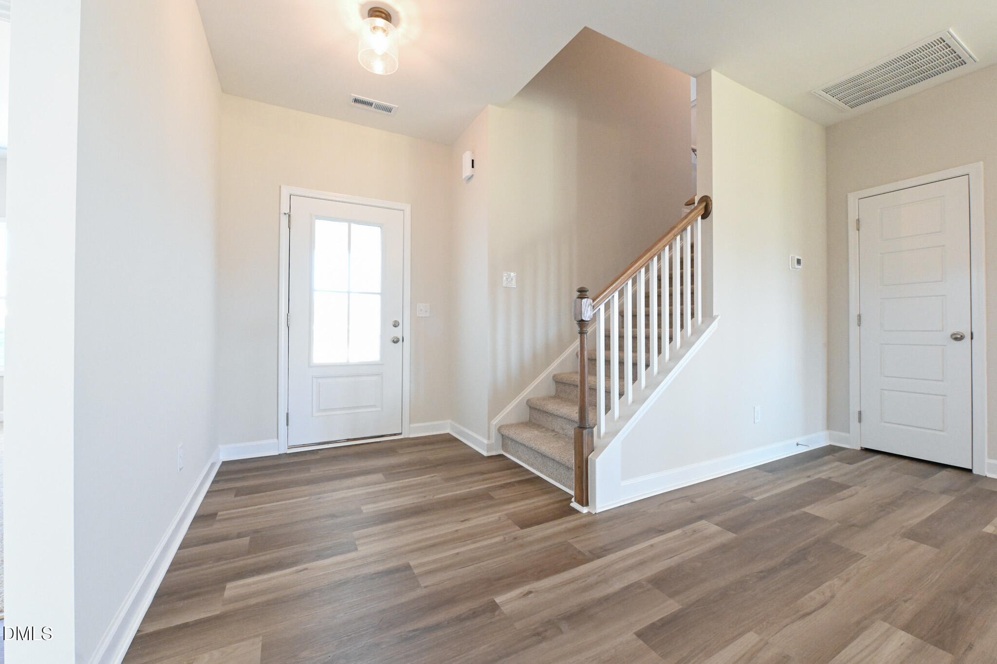 Entry foyer with plank flooring, a glass-panel front door, and carpeted staircase with wood handrail.