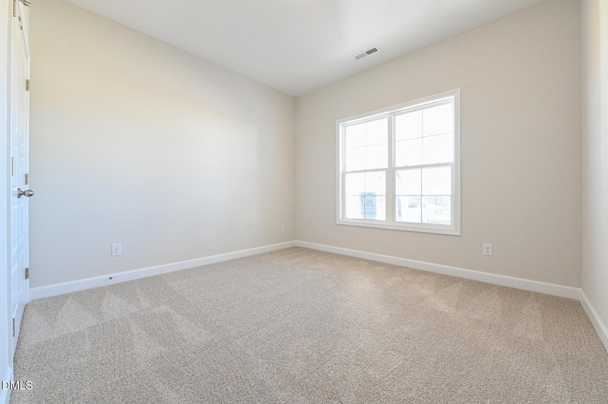Empty bedroom with beige carpet, a large double window, and white trim.