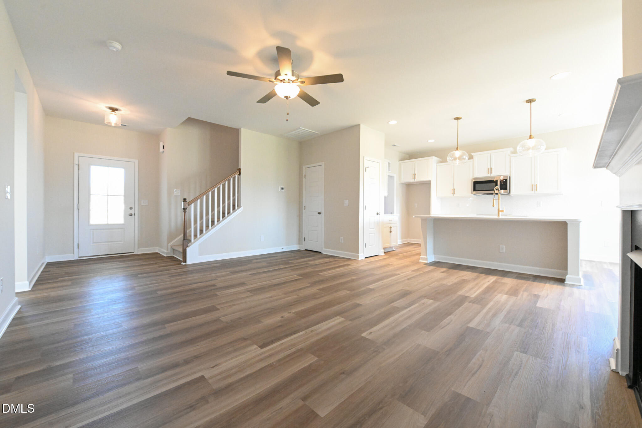 Open-plan living room and kitchen with plank flooring, a staircase, white cabinets, and a large island.