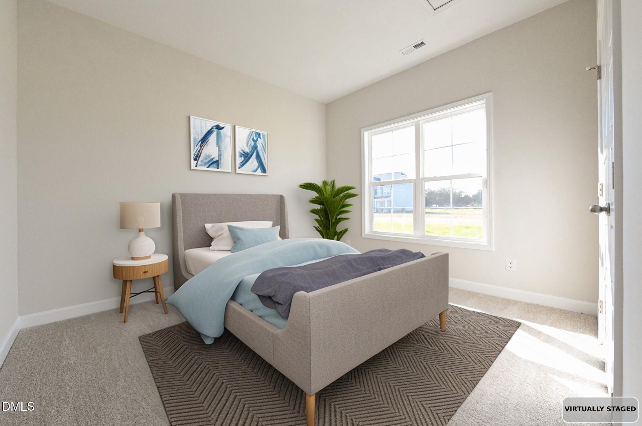 Virtually staged bedroom with a gray upholstered bed, blue bedding, patterned rug, and large sunlit window.