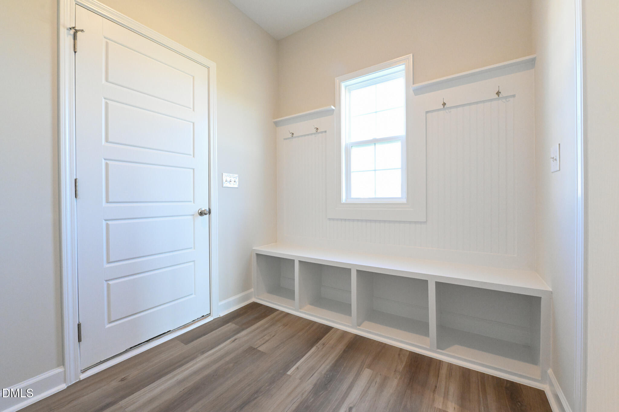 Bright mudroom with a built-in white bench, open cubbies, coat hooks, and a window.