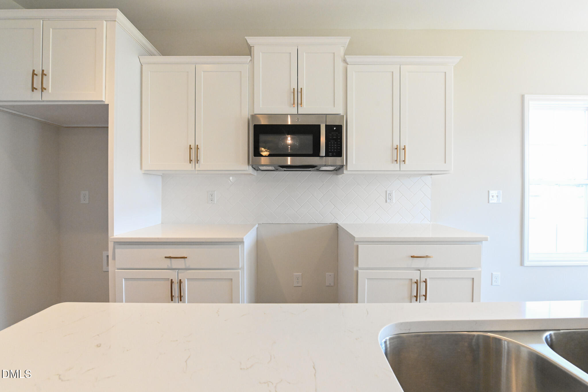 Kitchen with white shaker cabinets, brass pulls, diagonal tile backsplash, and a quartz island with sink.