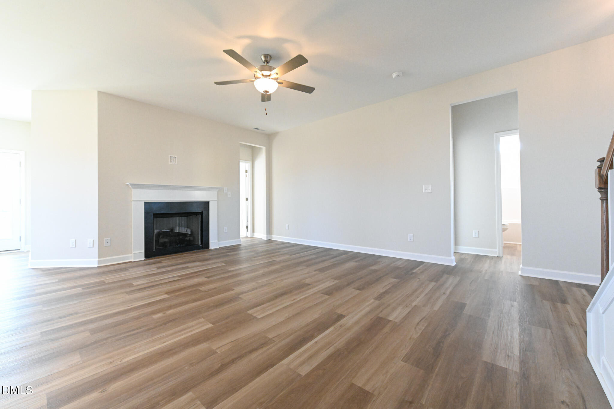 Empty living room with a white-trimmed fireplace, wood-look floors, and a lit ceiling fan.