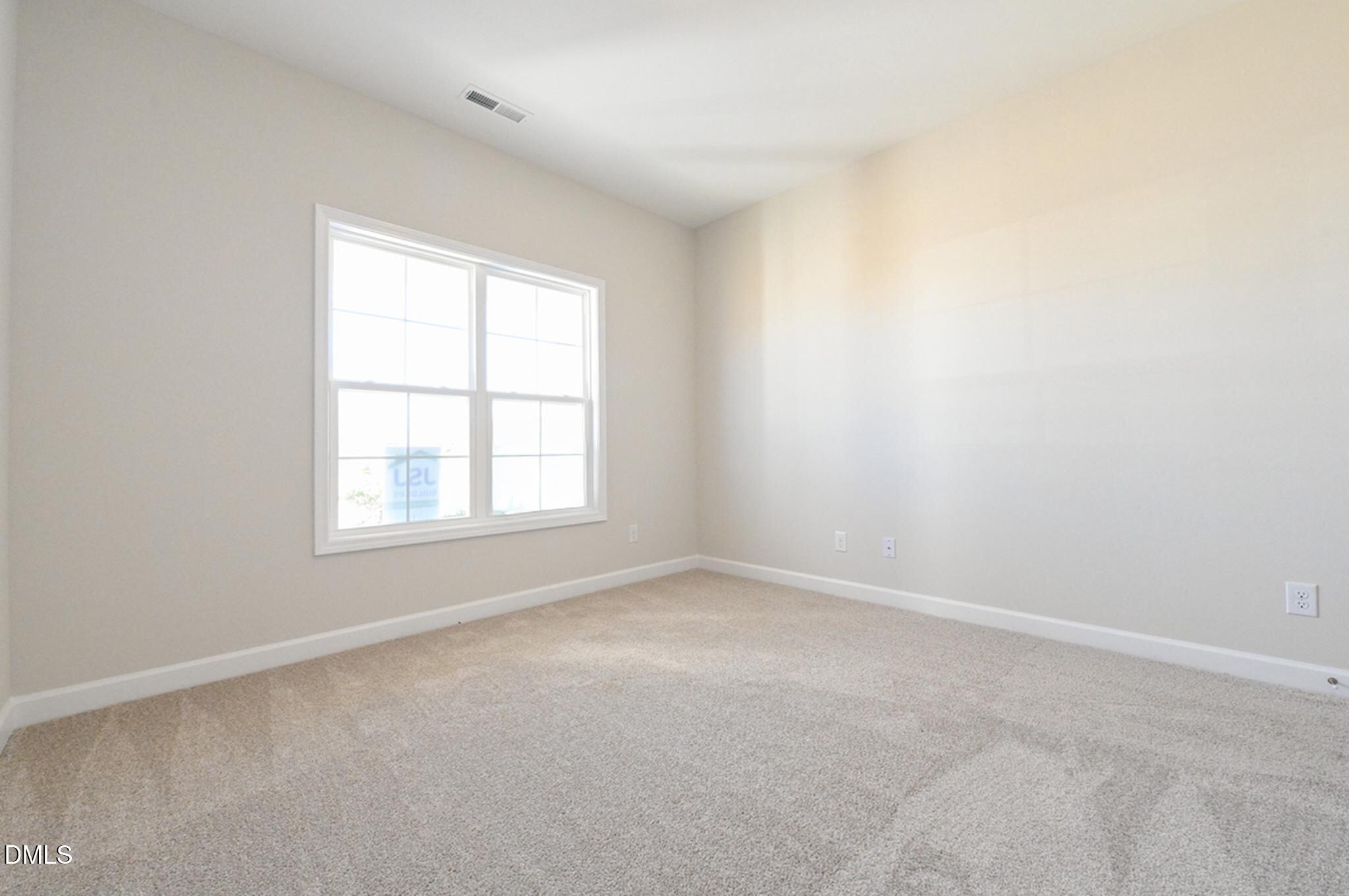 Empty bedroom with beige carpet and a large divided window.