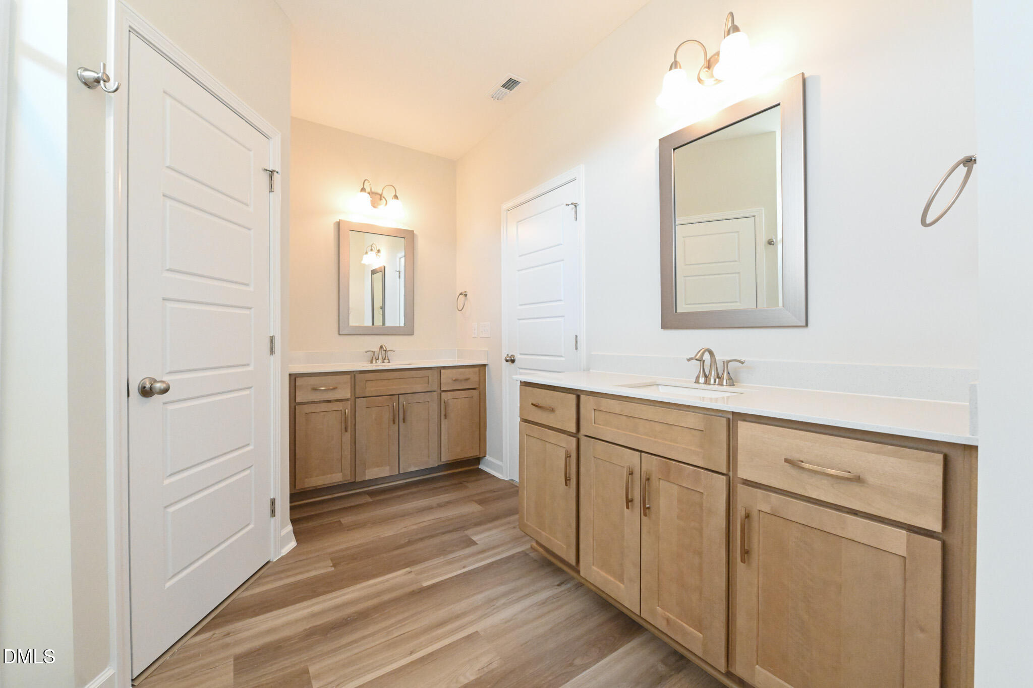 Bathroom with two wood vanities, white countertops, framed mirrors, and wood-look plank flooring.