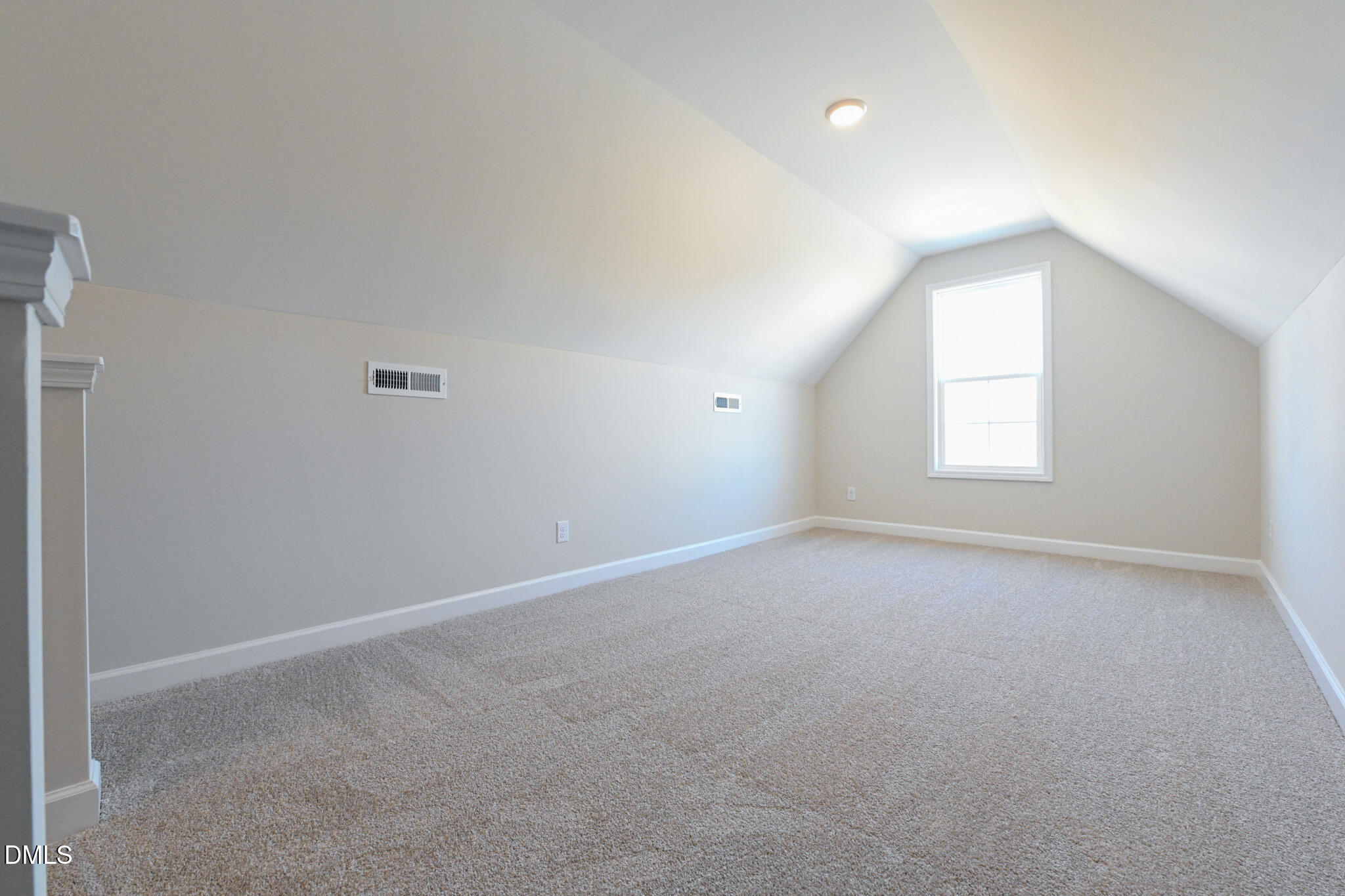 Empty carpeted upper-level room with a steeply sloped ceiling and single window.