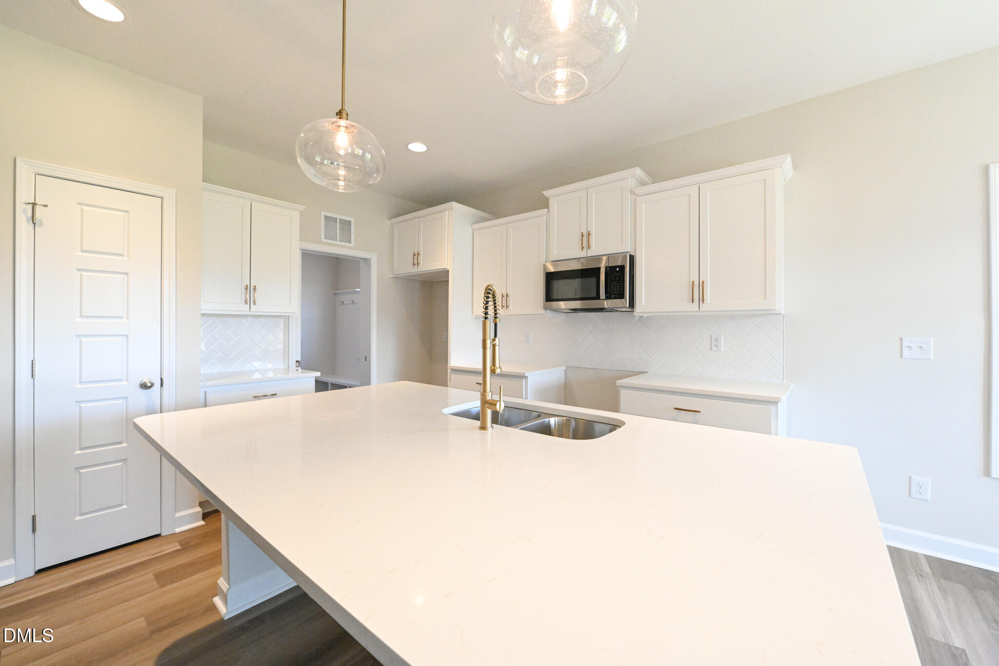 Vacant kitchen with a large island, white shaker cabinets, and a gold-tone faucet.