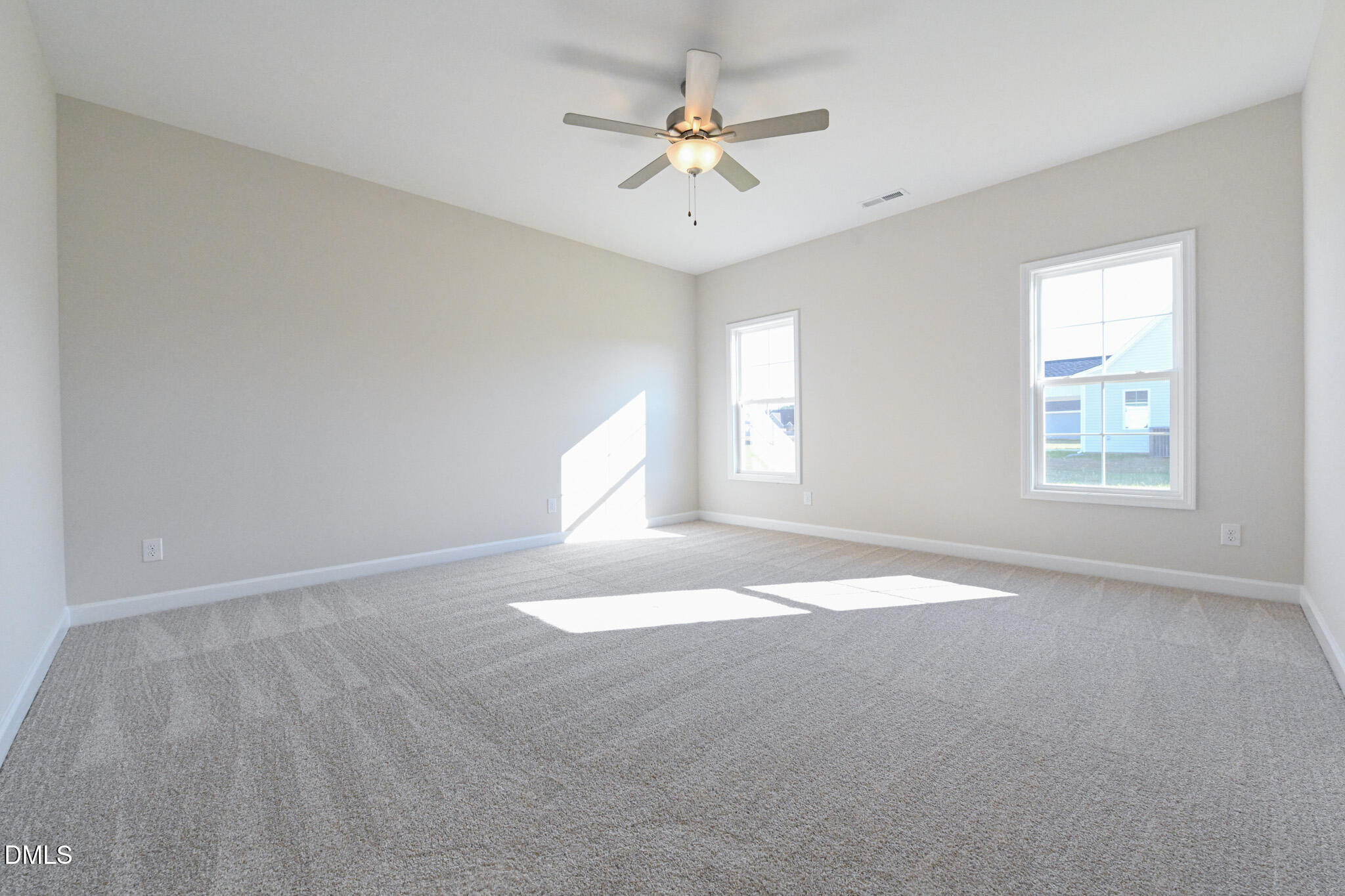 Empty carpeted bedroom with a ceiling fan and two sunlit windows.