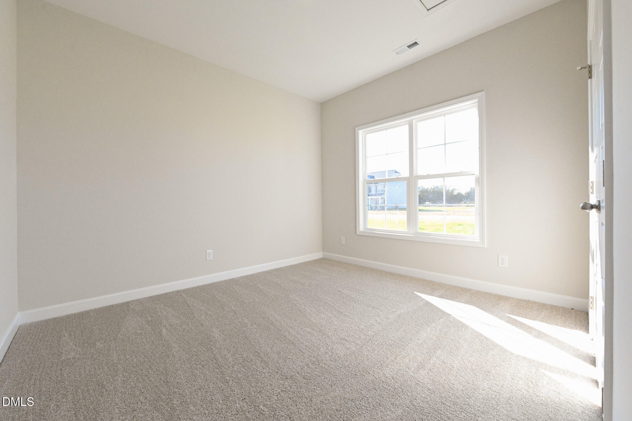Empty carpeted room with beige walls and a large sunlit window.