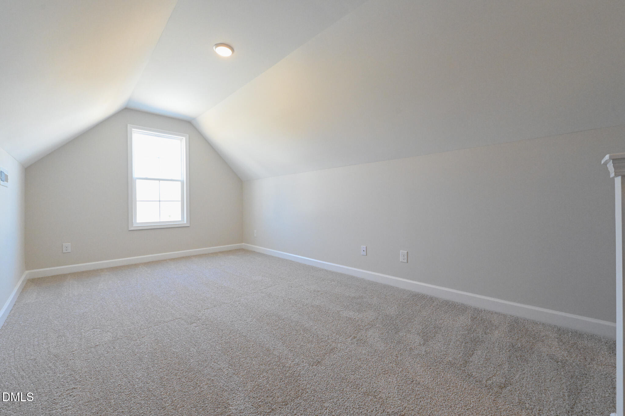 Empty carpeted upstairs room with a sloped ceiling and one window.