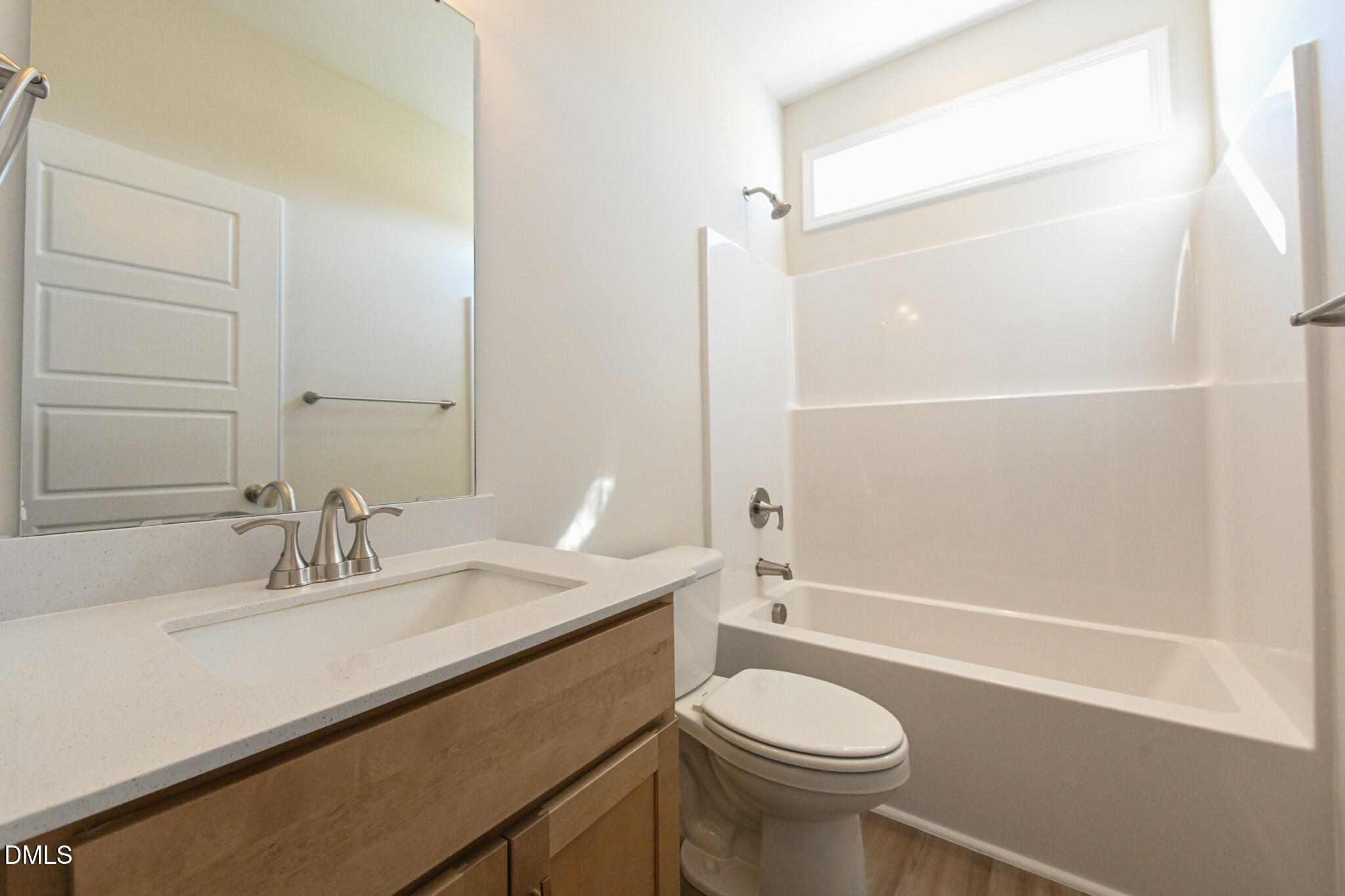 Bathroom with a wood vanity, large mirror, and white tub and shower beneath a high window.