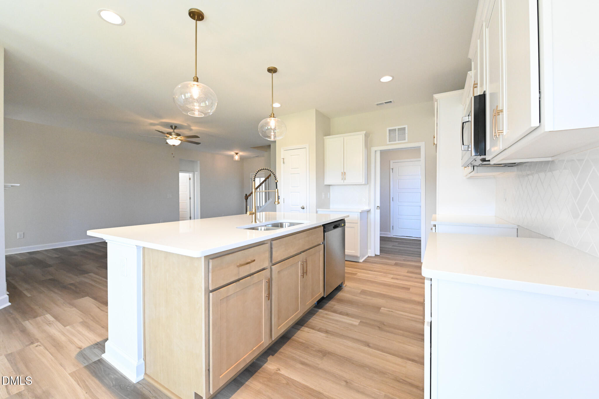 Vacant kitchen with a large island, brass-tone faucet, light wood cabinets, and pendant lights.