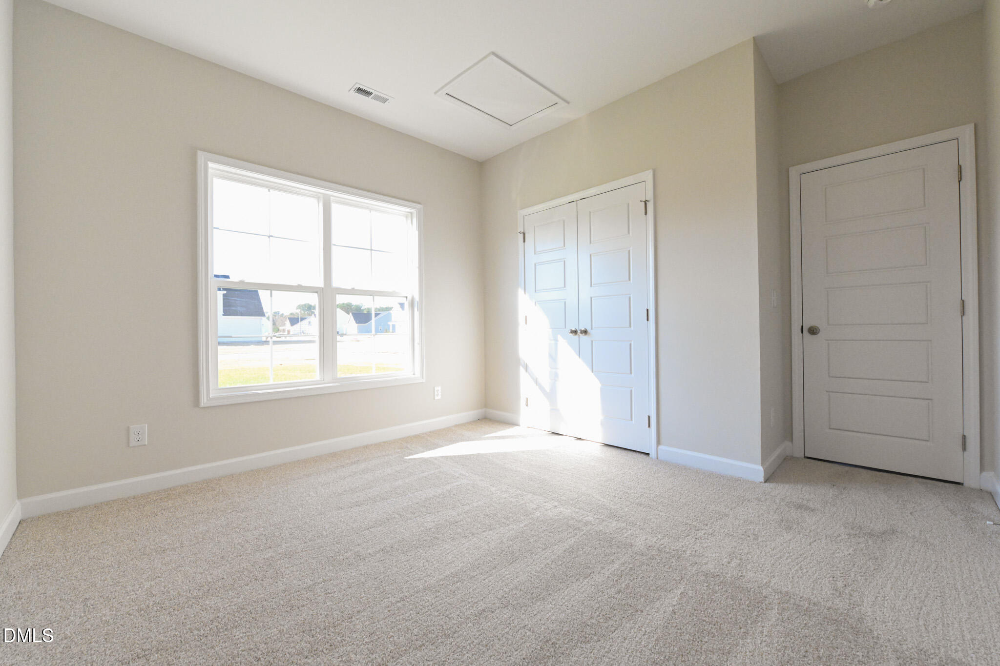 Empty carpeted bedroom with a large window and double closet doors.