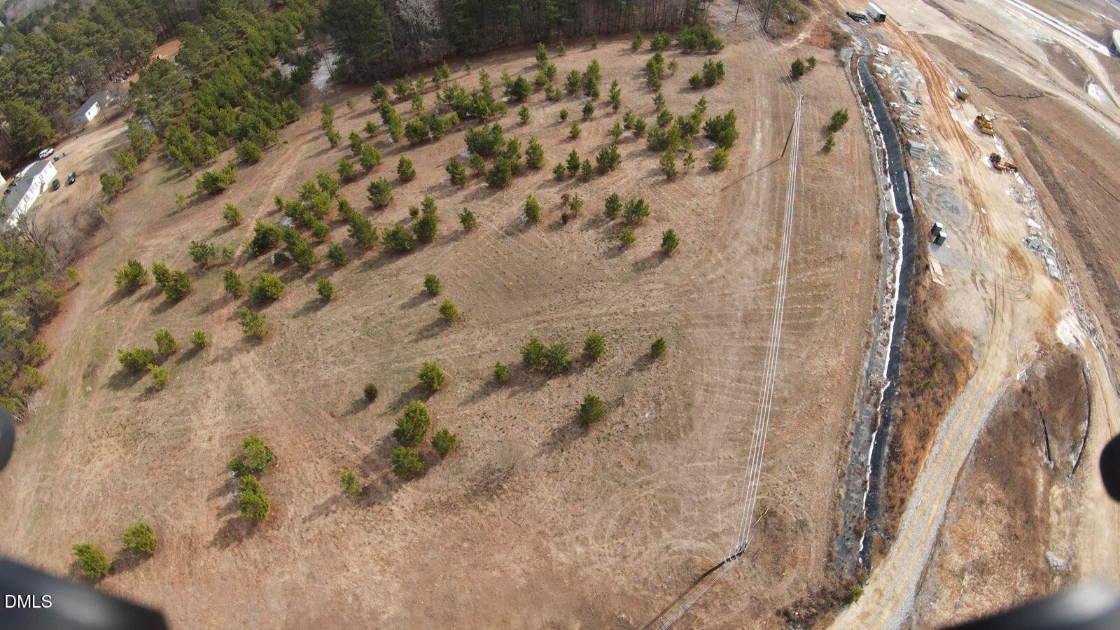 Aerial view of open land with scattered evergreen trees beside a graded construction area.