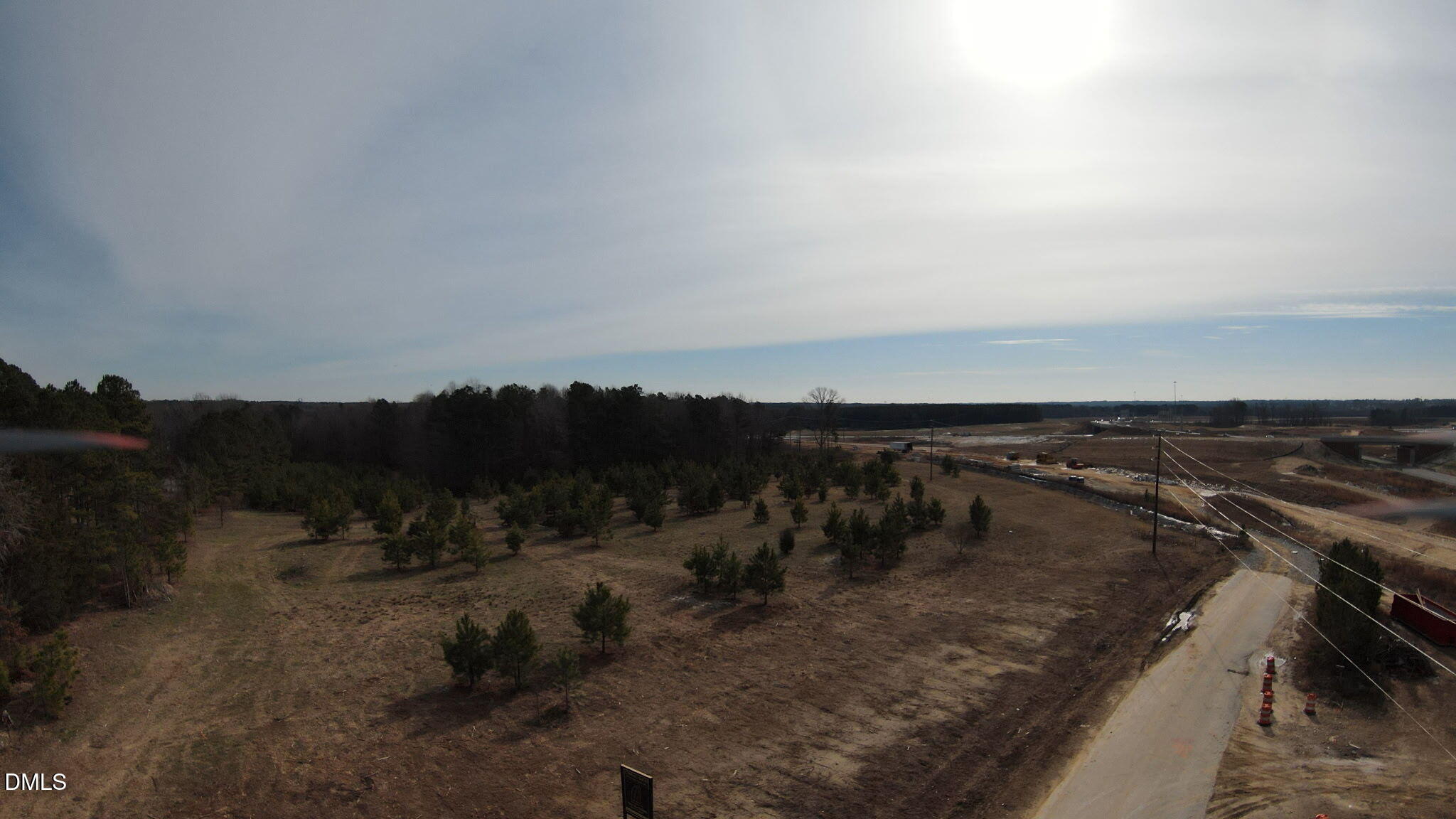 Aerial view of open land with scattered pines beside a road and nearby construction.