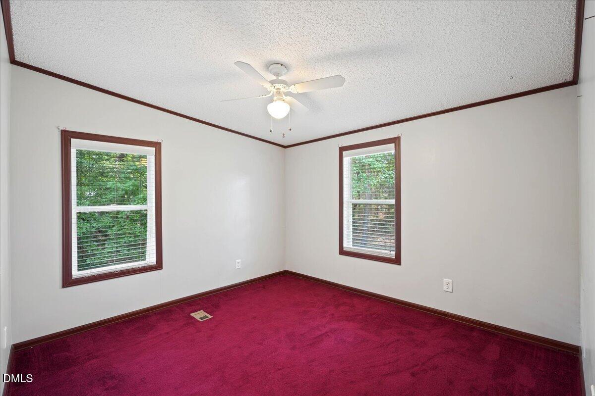 Empty bedroom with burgundy carpet, two windows, and a ceiling fan with light.