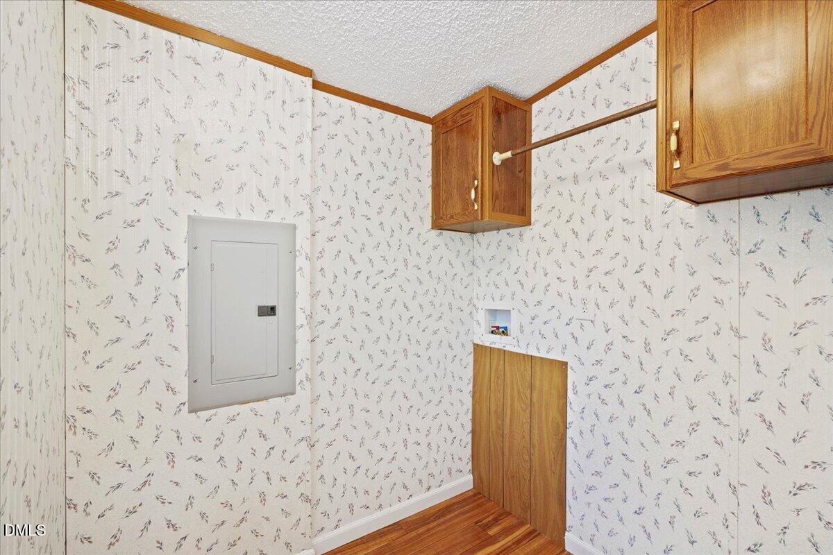 Utility room with floral wallpaper, wood cabinets, a hanging rod, and an electrical panel.