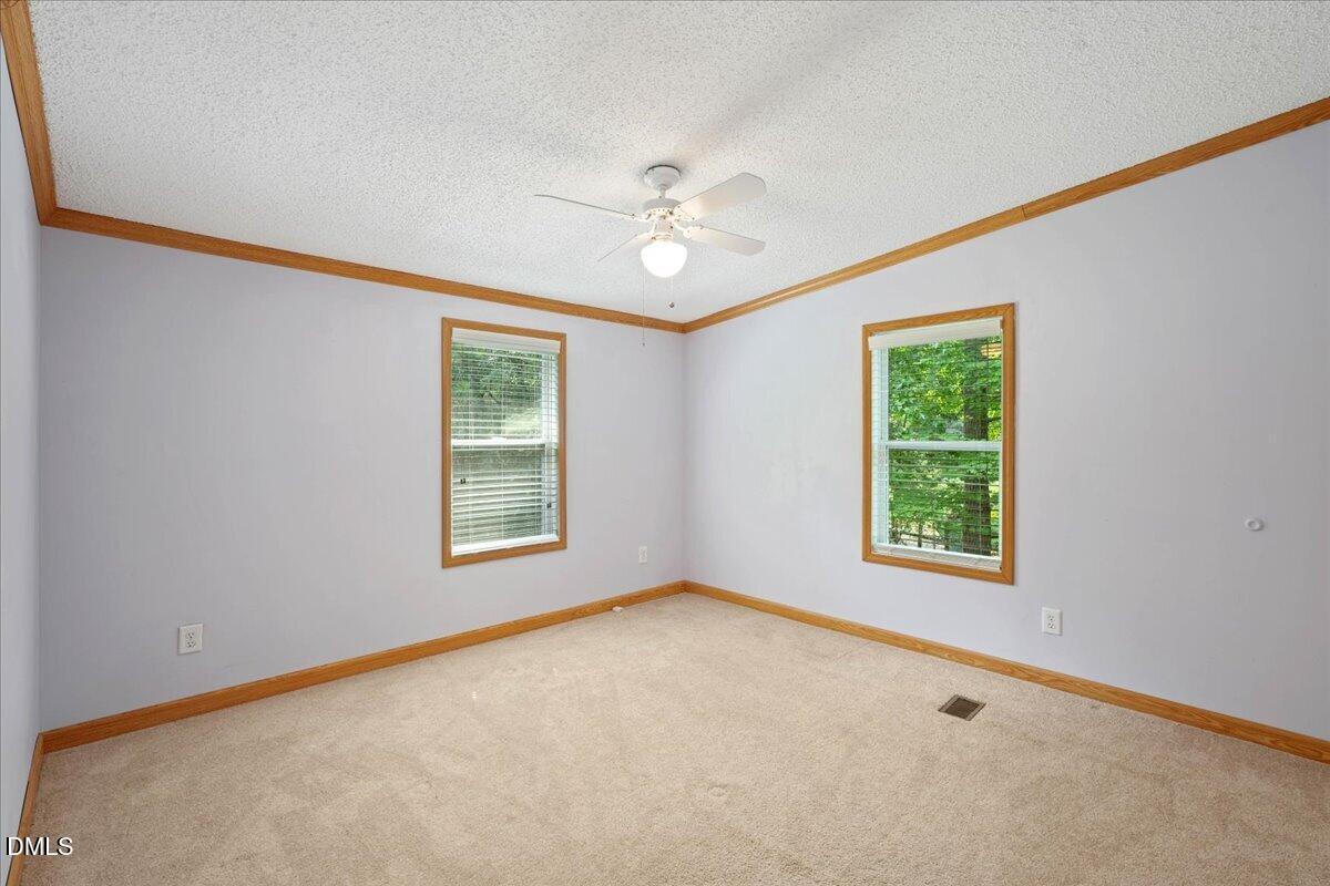 Empty carpeted room with two windows, warm wood trim, and a ceiling fan.