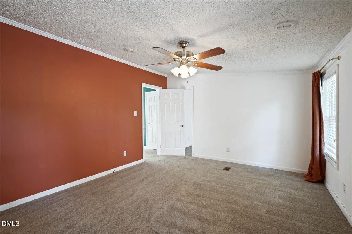 Empty bedroom with beige carpet, a rust-red accent wall, and a ceiling fan.
