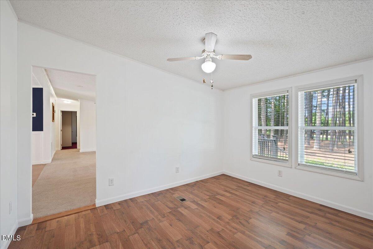Unfurnished room with wood-look flooring, a ceiling fan, and two windows overlooking trees.