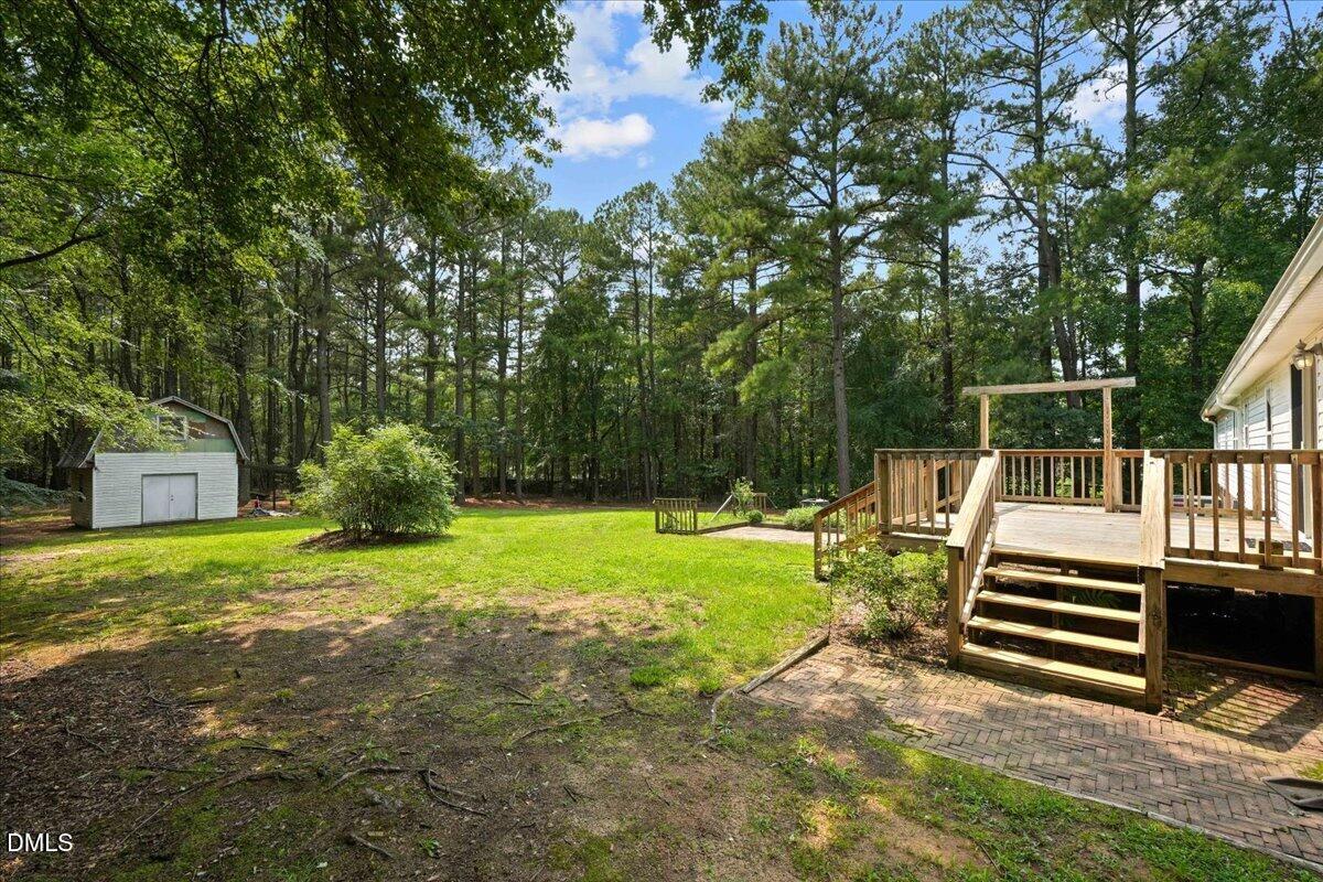 Backyard with a raised wooden deck, brick patio, grassy lawn, and shed surrounded by mature trees.