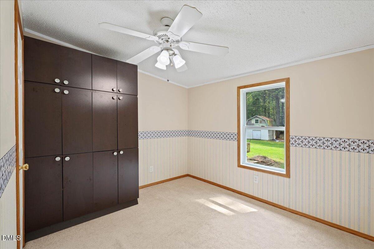 Unfurnished bedroom with dark built-in cabinets, a ceiling fan, and a window overlooking the yard.
