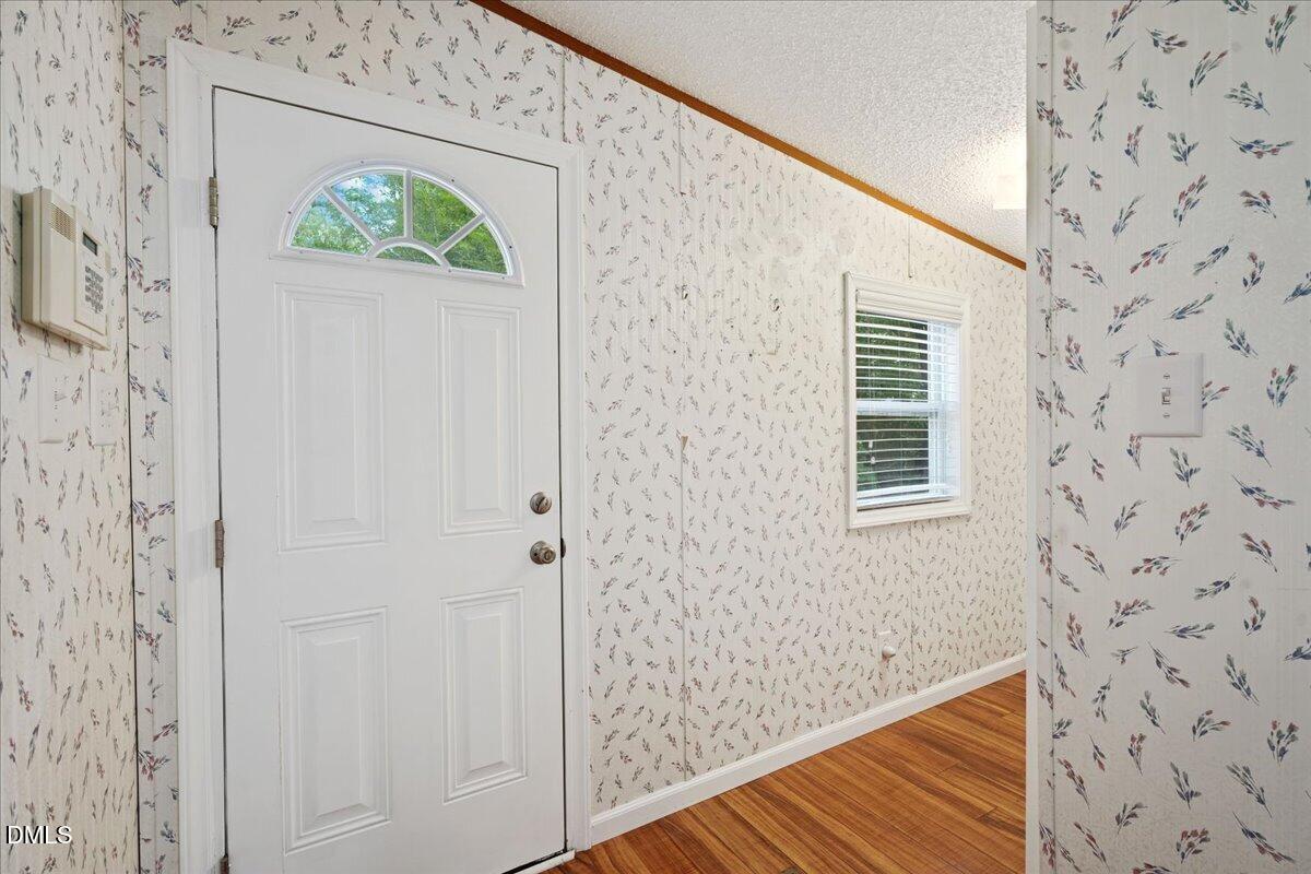 Entry hall with a white front door, floral wallpaper, and hardwood flooring.