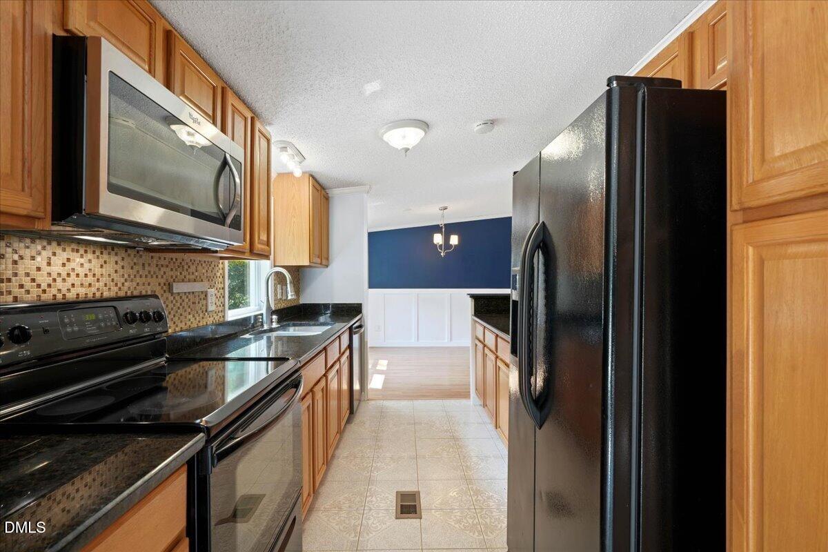 Kitchen with wood cabinets, dark countertops, black appliances, and a mosaic tile backsplash.