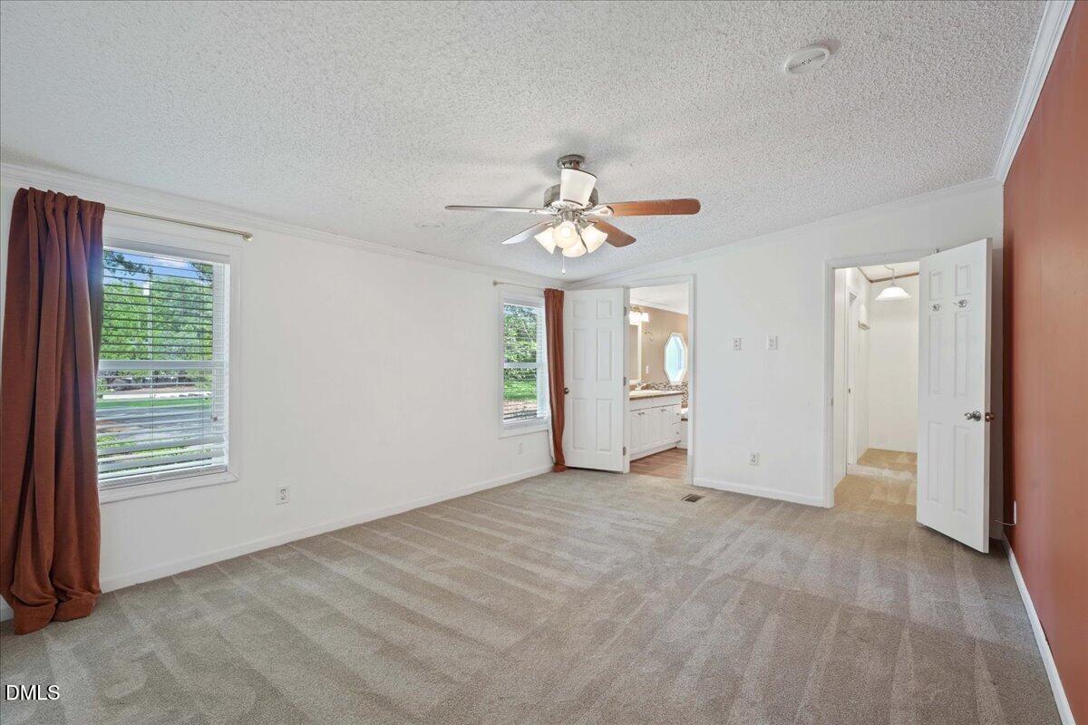 Unfurnished bedroom with beige patterned carpet, burgundy curtains, and a ceiling fan.
