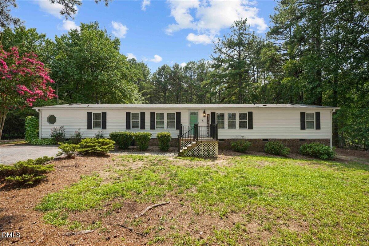 Long white single-story home with dark shutters and a small front porch, surrounded by trees.
