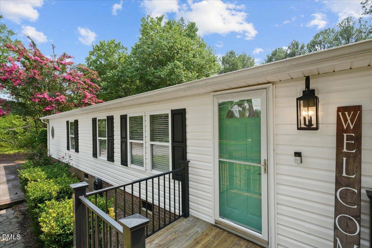 Home entrance with a turquoise door, wooden porch, black railings, and pink flowering tree.