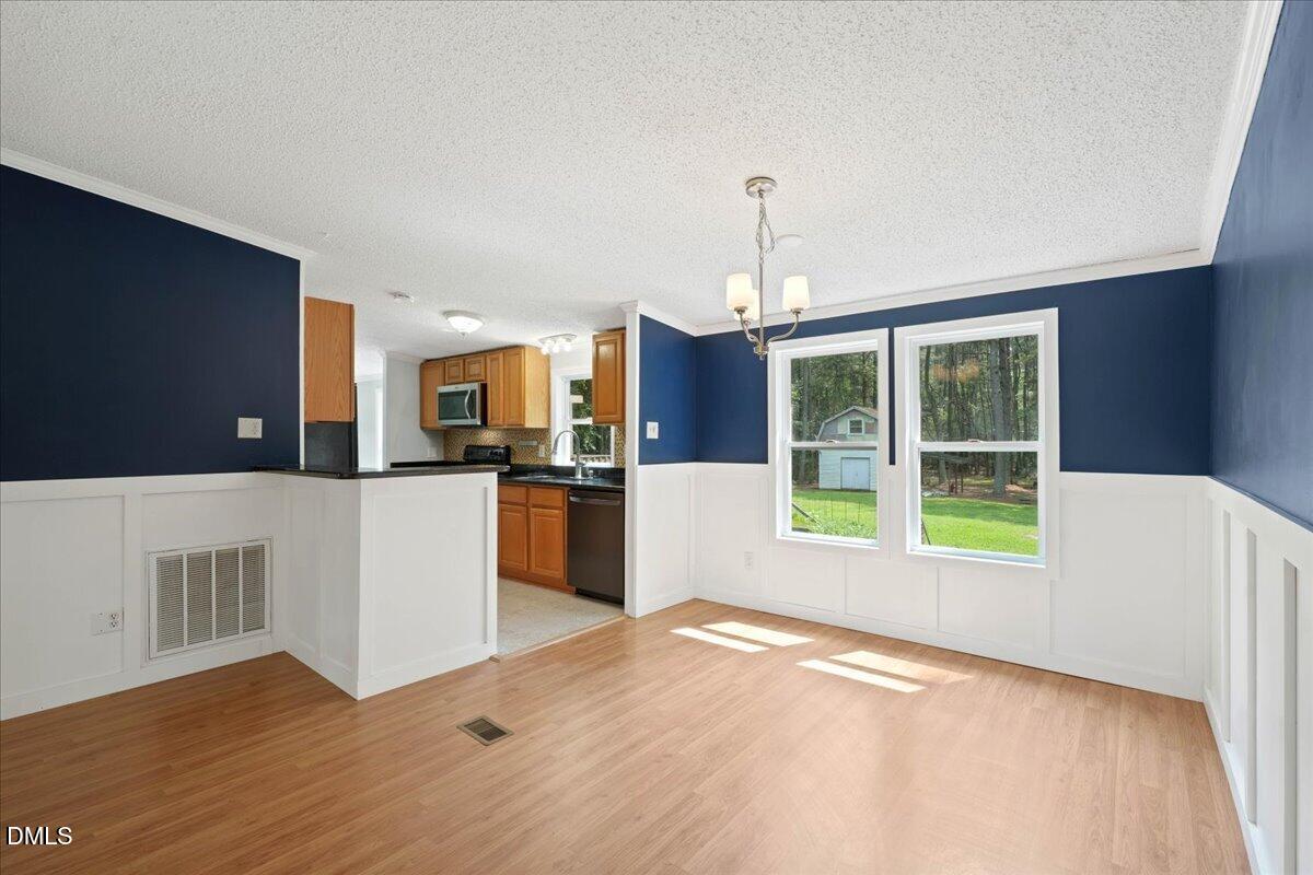 Vacant dining area with blue walls, white wainscoting, wood floors, and windows overlooking trees.