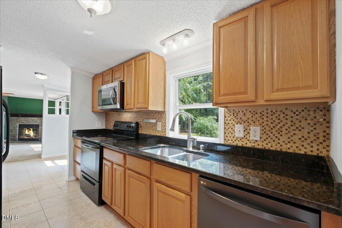 Kitchen with wood cabinets, granite counters, mosaic backsplash, and a double-basin sink beneath a window.
