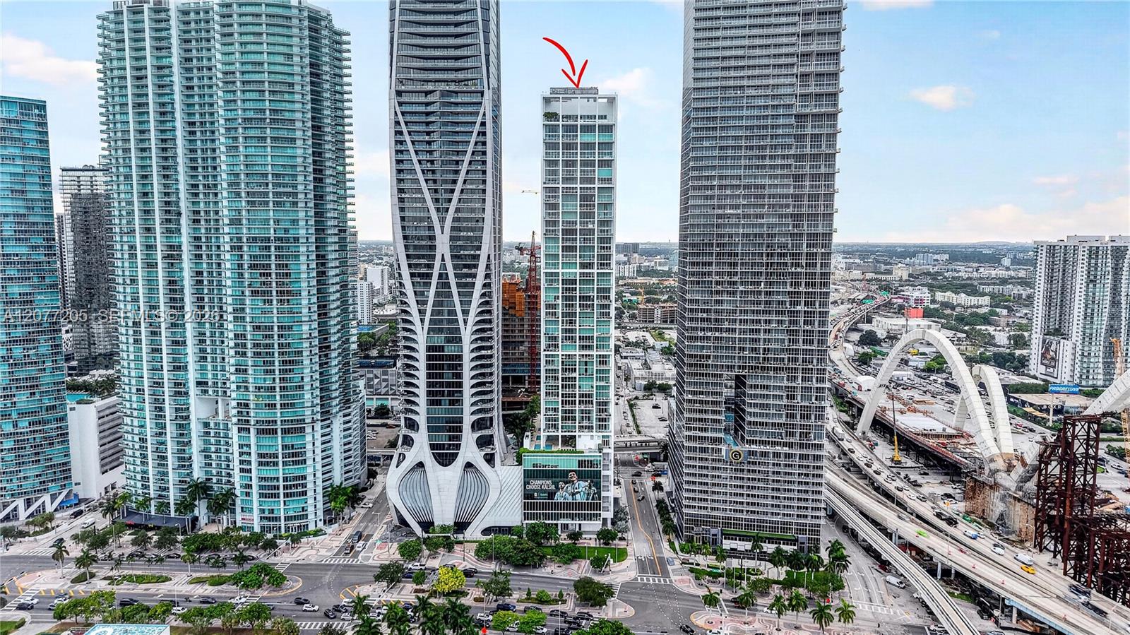 Downtown Miami skyline with a red arrow pointing to a white tower beside a bridge under construction.