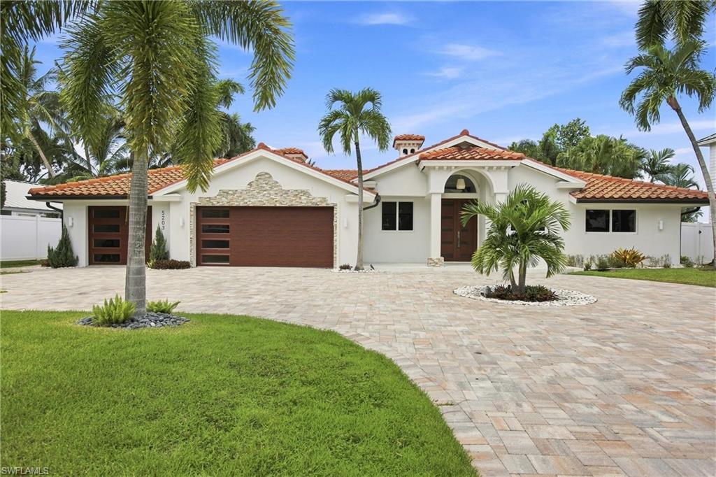 Single-story stucco home with a red tile roof, double garage, paver driveway, and palm trees.