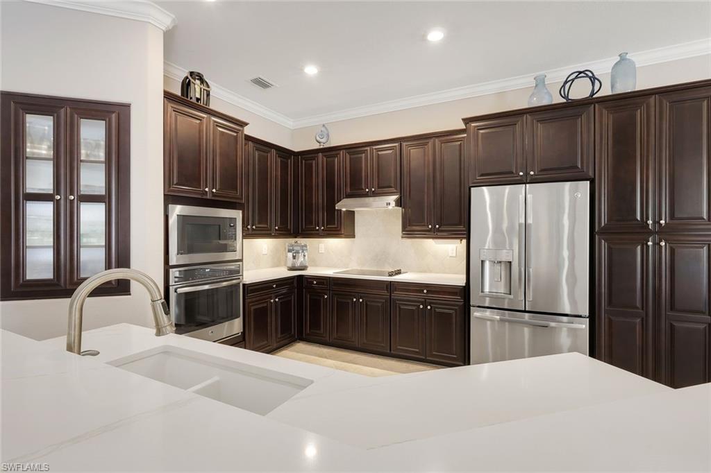 Kitchen with dark wood cabinets, stainless steel appliances, and a white island with an integrated sink.