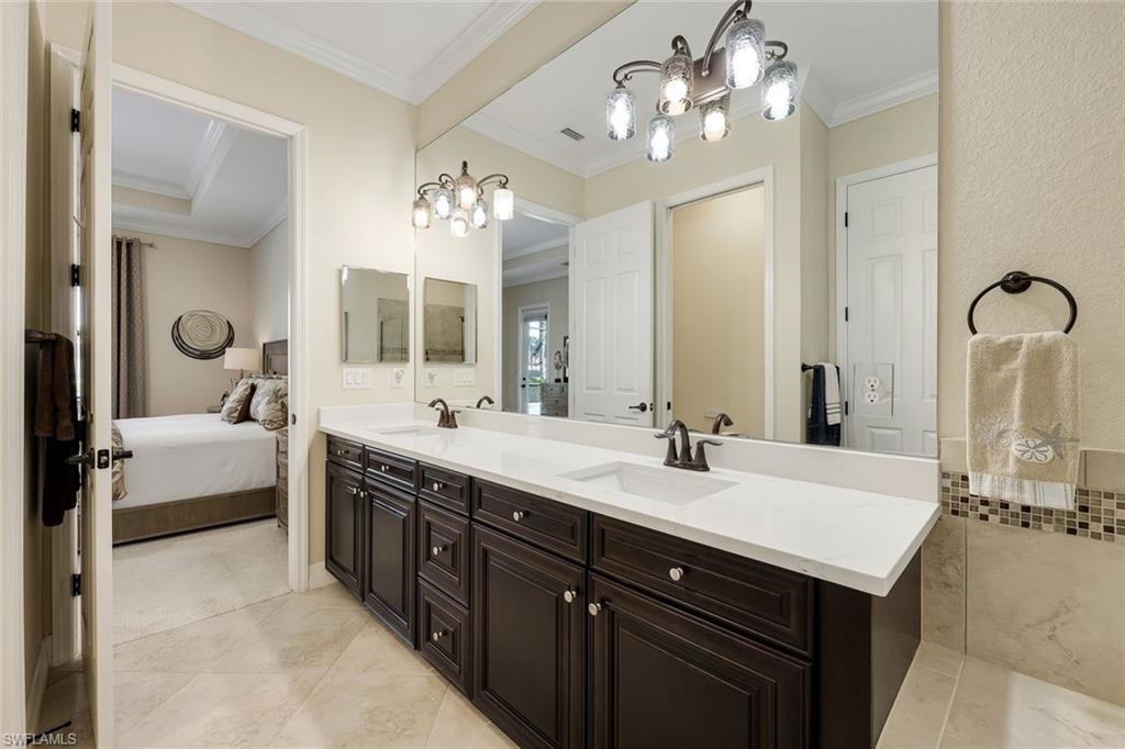 Primary bathroom with a dark double vanity, white countertop, and adjoining bedroom visible through the doorway.