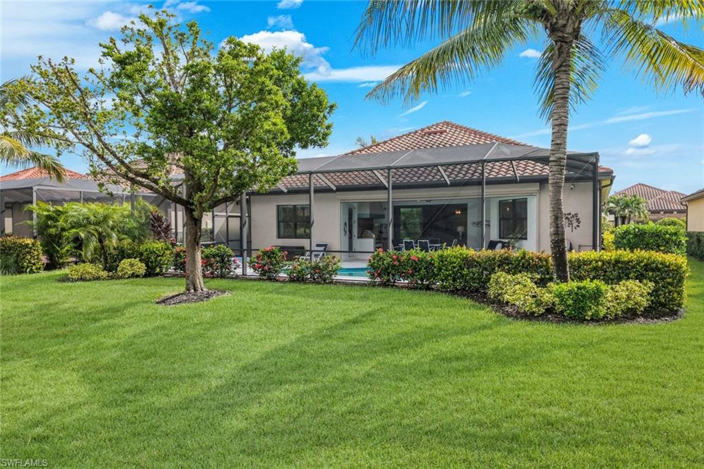 Home’s rear exterior with screened lanai, pool, palm trees, and a broad green lawn.