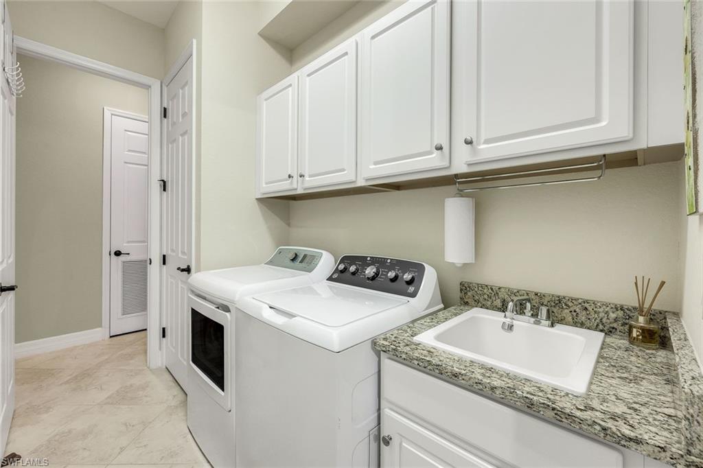 Laundry room with white washer and dryer, utility sink, granite countertop, and wall cabinets.