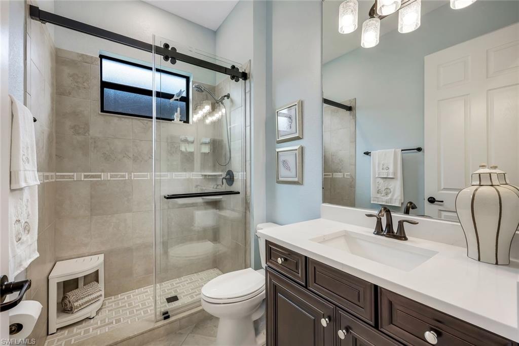 Bathroom with a glass-enclosed tiled shower, high window, and dark wood vanity.