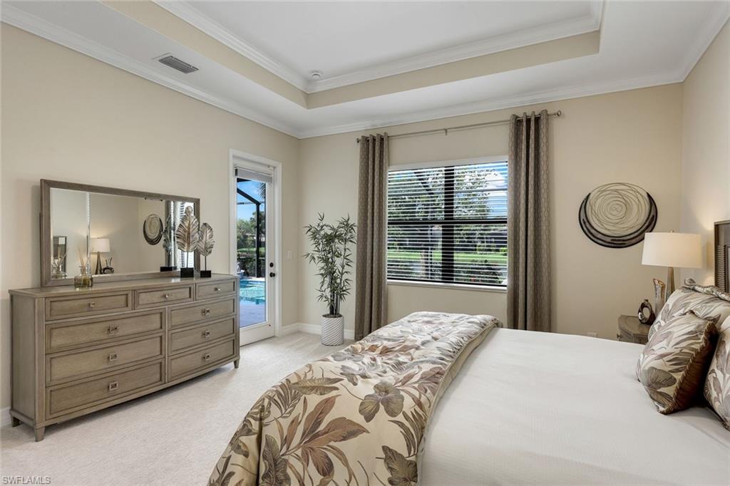 Bedroom with floral bedding, mirrored dresser, tray ceiling, and window overlooking greenery.